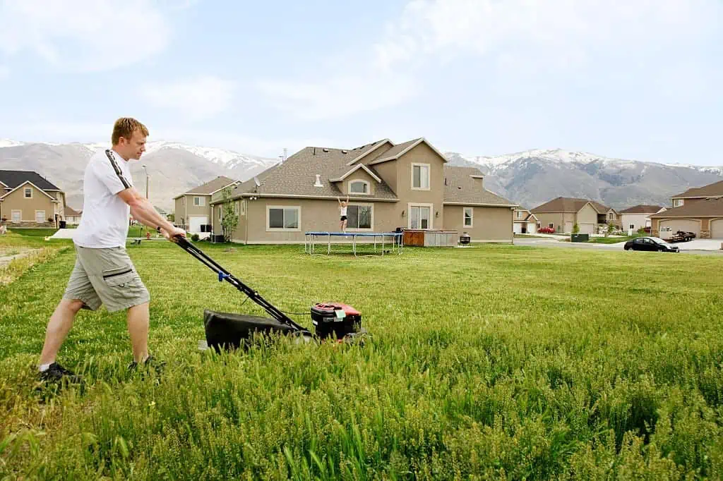 man mowing tall grass near trampoline